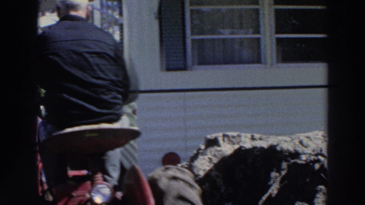 Man seen from behind near red tractor-like machinery beside a white mobile home in 1966 Puerto Rico footage.