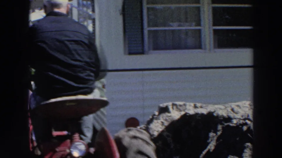 Man seen from behind near red tractor-like machinery beside a white mobile home in 1966 Puerto Rico footage.