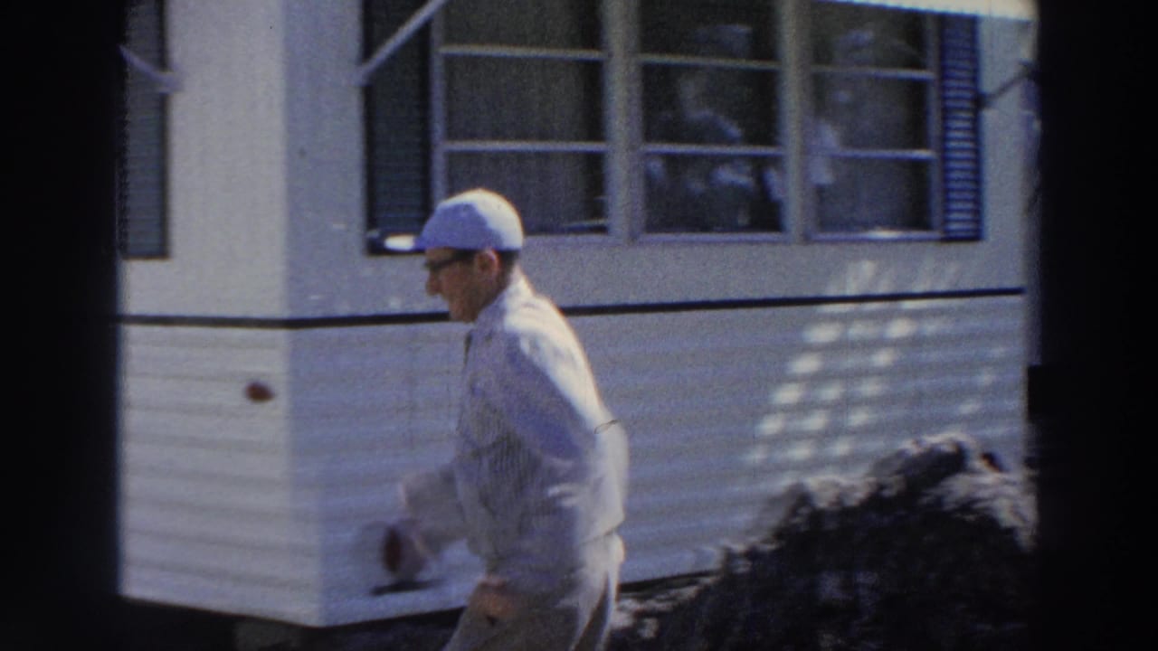 Man in a cap walking beside a white mobile home.