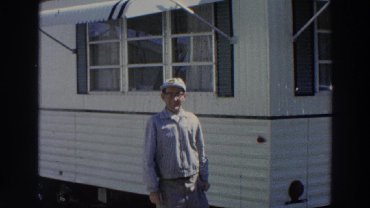 Man in a white cap and glasses stands outside a white mobile home.