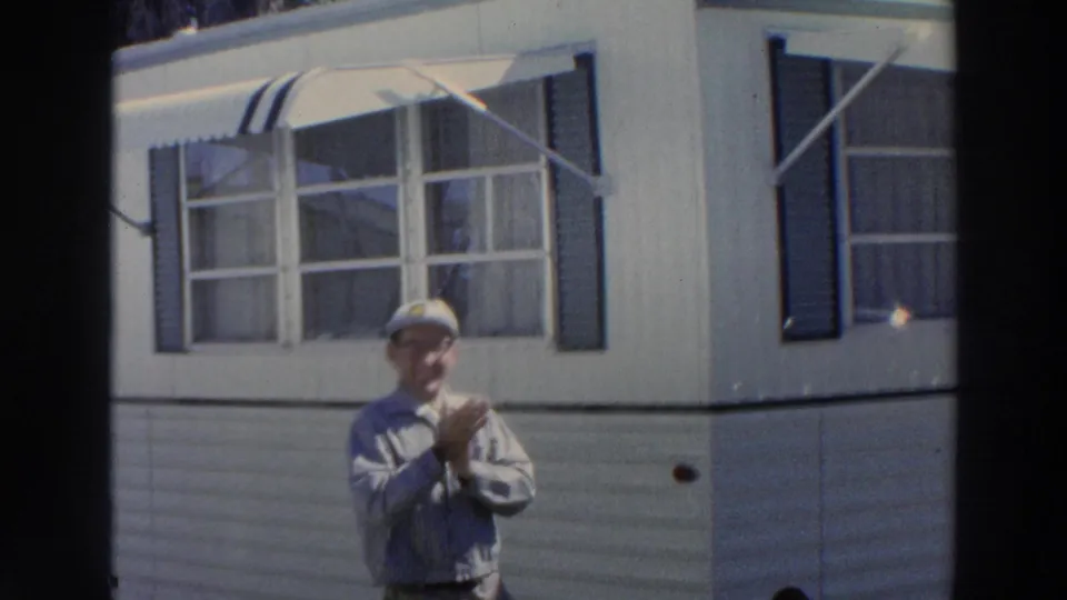 In Puerto Rico, 1966, a man in glasses and a white cap stands with hands together below a window and striped awning.