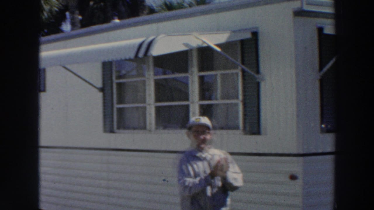 In Puerto Rico, 1966, the man remains outside the white mobile home, partly low in frame, with windows and an awning behind him.