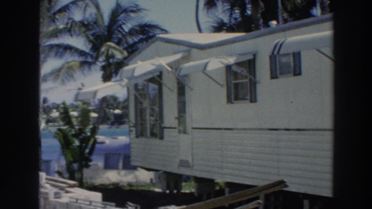 A 1966 Puerto Rico home-movie view shows a white mobile home with open windows, striped awnings, palm trees, and blue water beyond it.