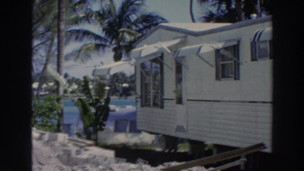 Tan mobile home with awnings and palm trees in bright daylight.