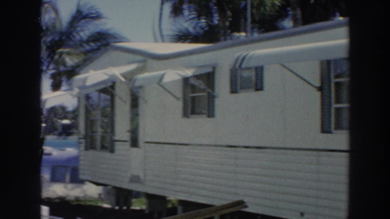 Side view of a tan mobile home with awnings and palms behind it.