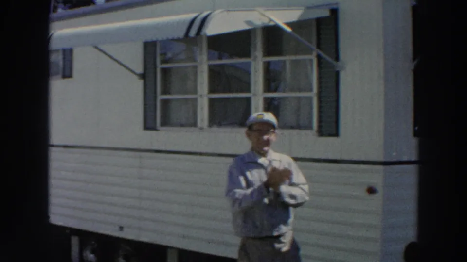 1966 Puerto Rico frame showing an adult man in a light blue shirt and cap standing near the corner of a tan mobile home.
