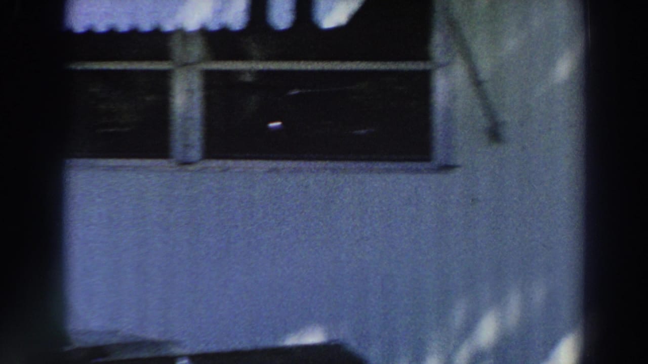 1966 Puerto Rico 8mm frame showing a close mobile-home wall, dark windows, awning edge, porch post, and soft tree shadows.