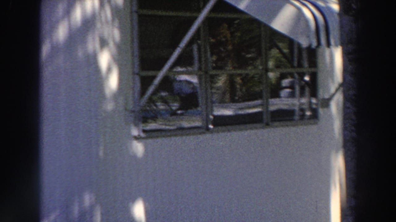 1966 Puerto Rico home-movie frame showing a mobile-home window, small porch railing, striped awning, siding, and dappled light.