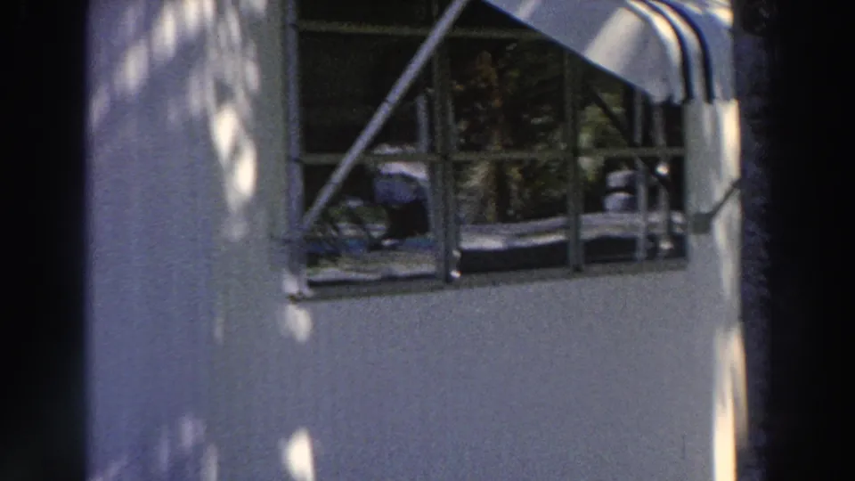 1966 Puerto Rico home-movie frame showing a mobile-home window, small porch railing, striped awning, siding, and dappled light.