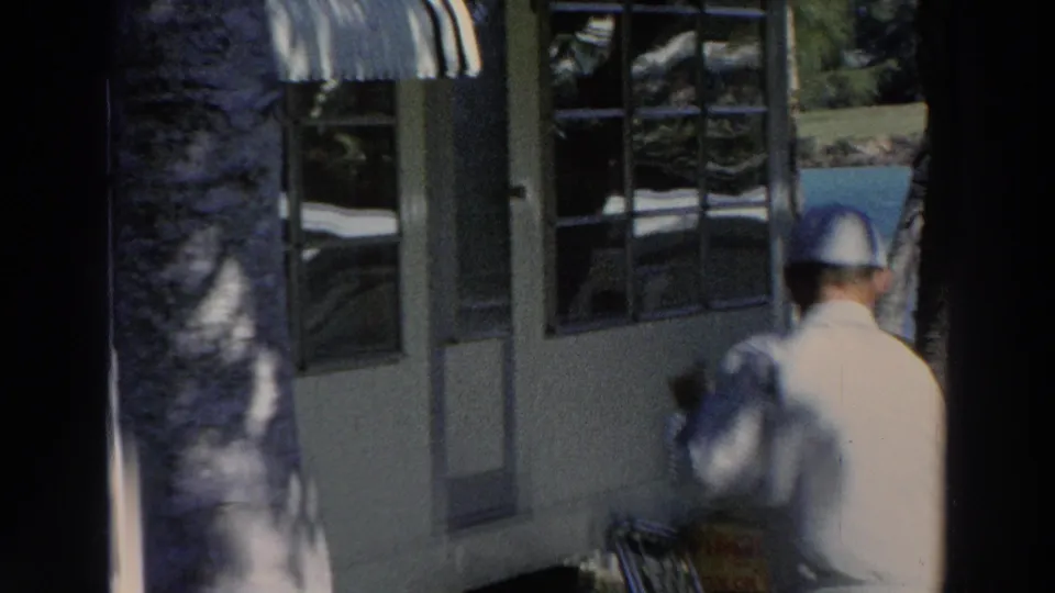 The man appears blurred as he mops near the building, with a dark foreground post or tree trunk dividing the 1966 Puerto Rico frame.
