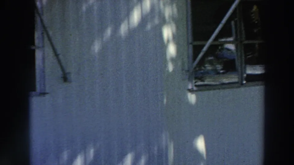 A Puerto Rico house exterior in dappled shade, with a window and dark vertical strip crossing the 8mm frame.