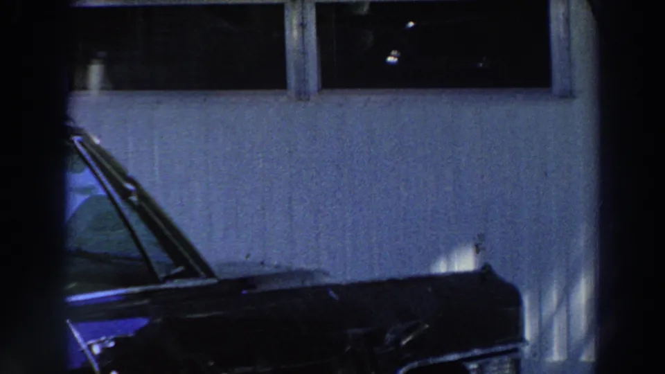 A dark blue car is partly visible outside a pale Puerto Rico house, with windows and soft palm shade in the frame.