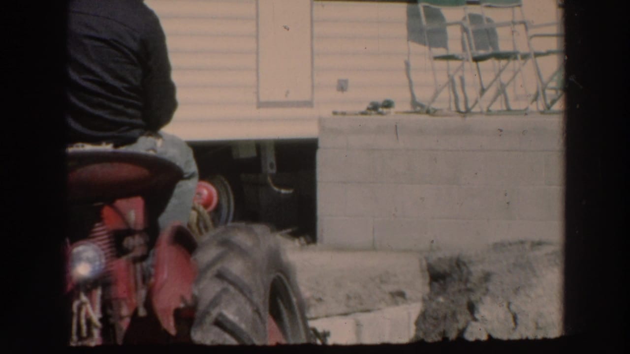 A man in a dark shirt rides a red tractor through a residential yard in 1966 Puerto Rico home-movie footage.