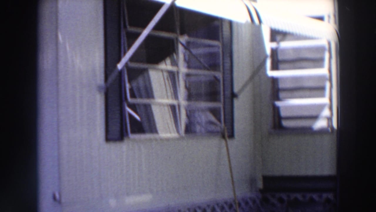 1966 Puerto Rico exterior view of a light-sided house with louvered windows, dark shutters, and striped awnings.