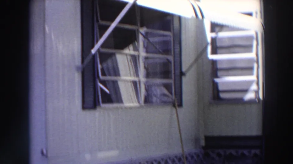 1966 Puerto Rico exterior view of a light-sided house with louvered windows, dark shutters, and striped awnings.