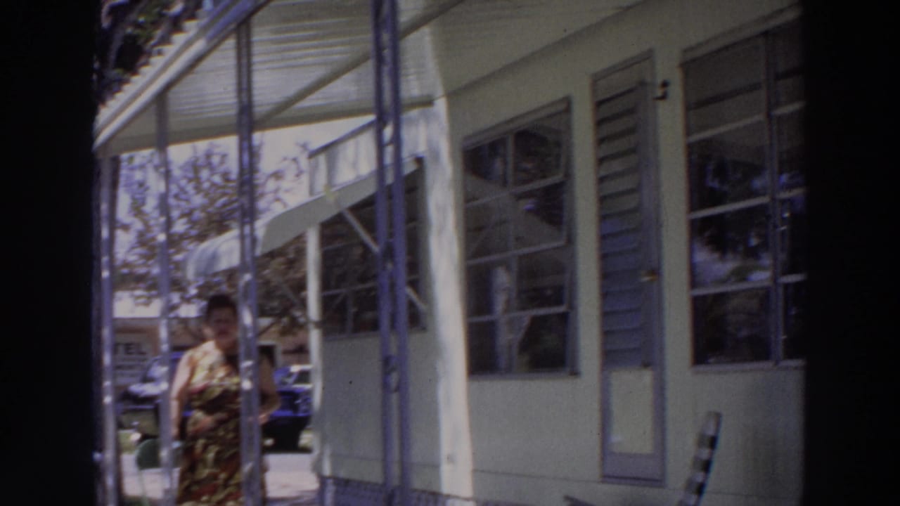 1966 Puerto Rico frame with a woman near a porch column, louvered windows, a door, and a parked car in the background.