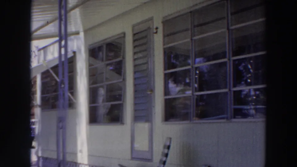 1966 Puerto Rico home-movie frame focused on the porch, windows, door, and pale exterior of the house.
