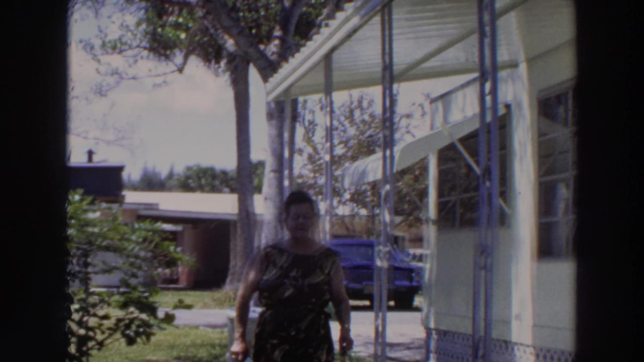 Woman walking closer to the camera on a porch with a blue car in the background.