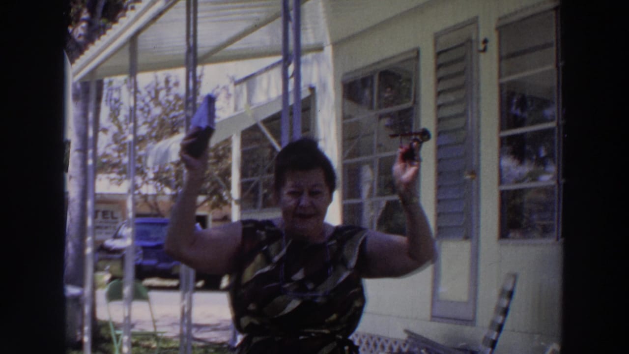 The woman smiles and lifts her handbag and sunglasses beside a screened porch in the 1966 Puerto Rico home-movie scene.