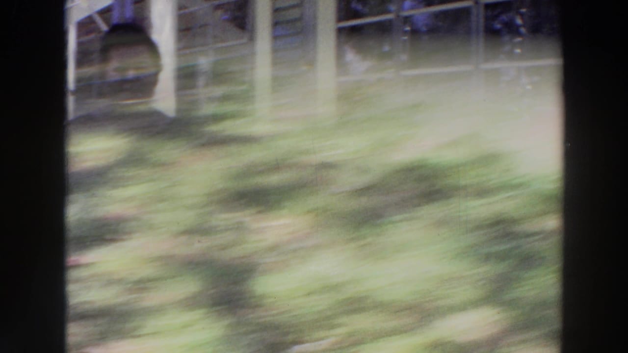 A motion-blurred 8mm frame shows grass, porch posts, and partial reflections as the camera shifts during the Puerto Rico exterior scene.
