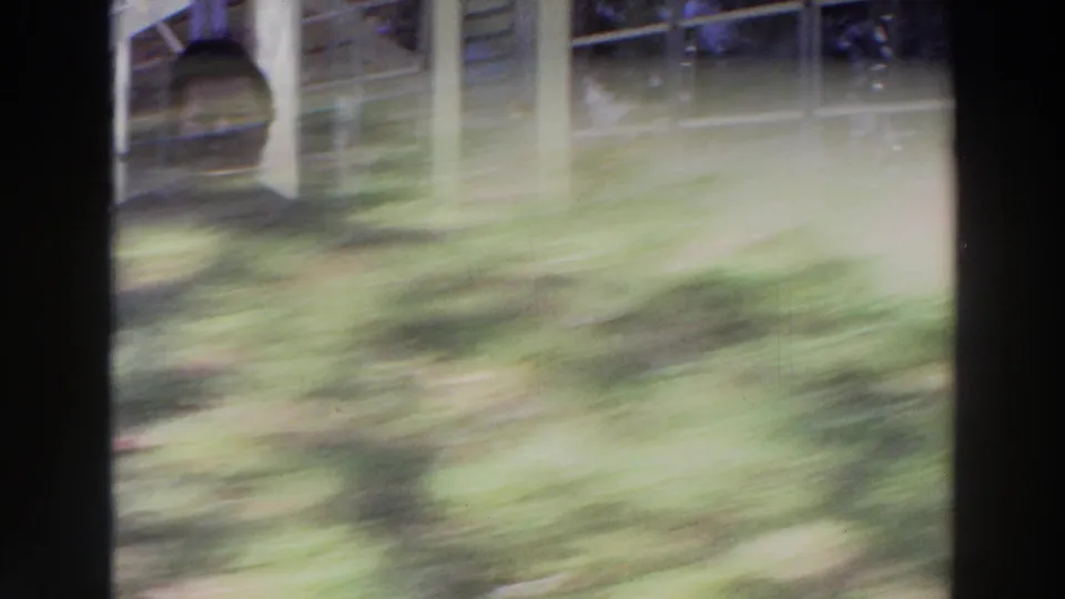 A motion-blurred 8mm frame shows grass, porch posts, and partial reflections as the camera shifts during the Puerto Rico exterior scene.