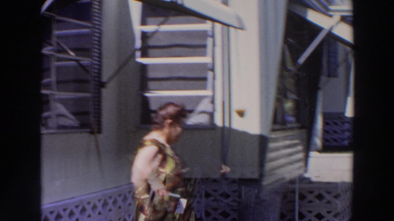 Older woman in a patterned dress stands beside a light-colored mobile home.