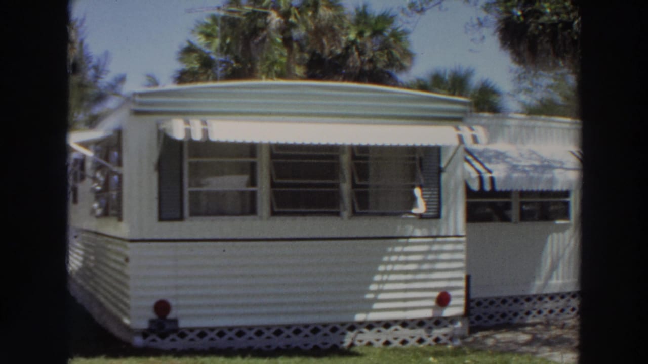 1966 Puerto Rico frame with a white trailer side, striped awnings, jalousie-style windows, lattice base, lawn, and palm trees.