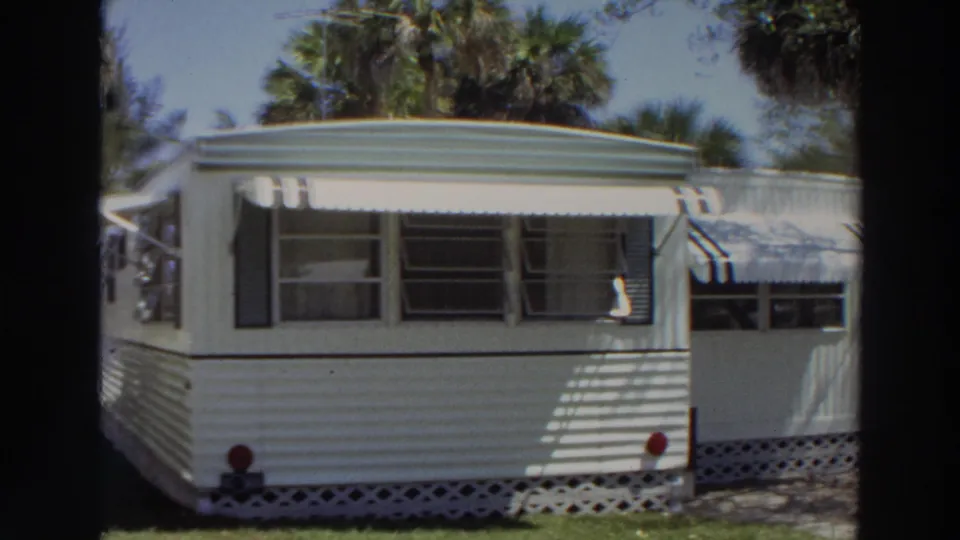 1966 Puerto Rico frame with a white trailer side, striped awnings, jalousie-style windows, lattice base, lawn, and palm trees.