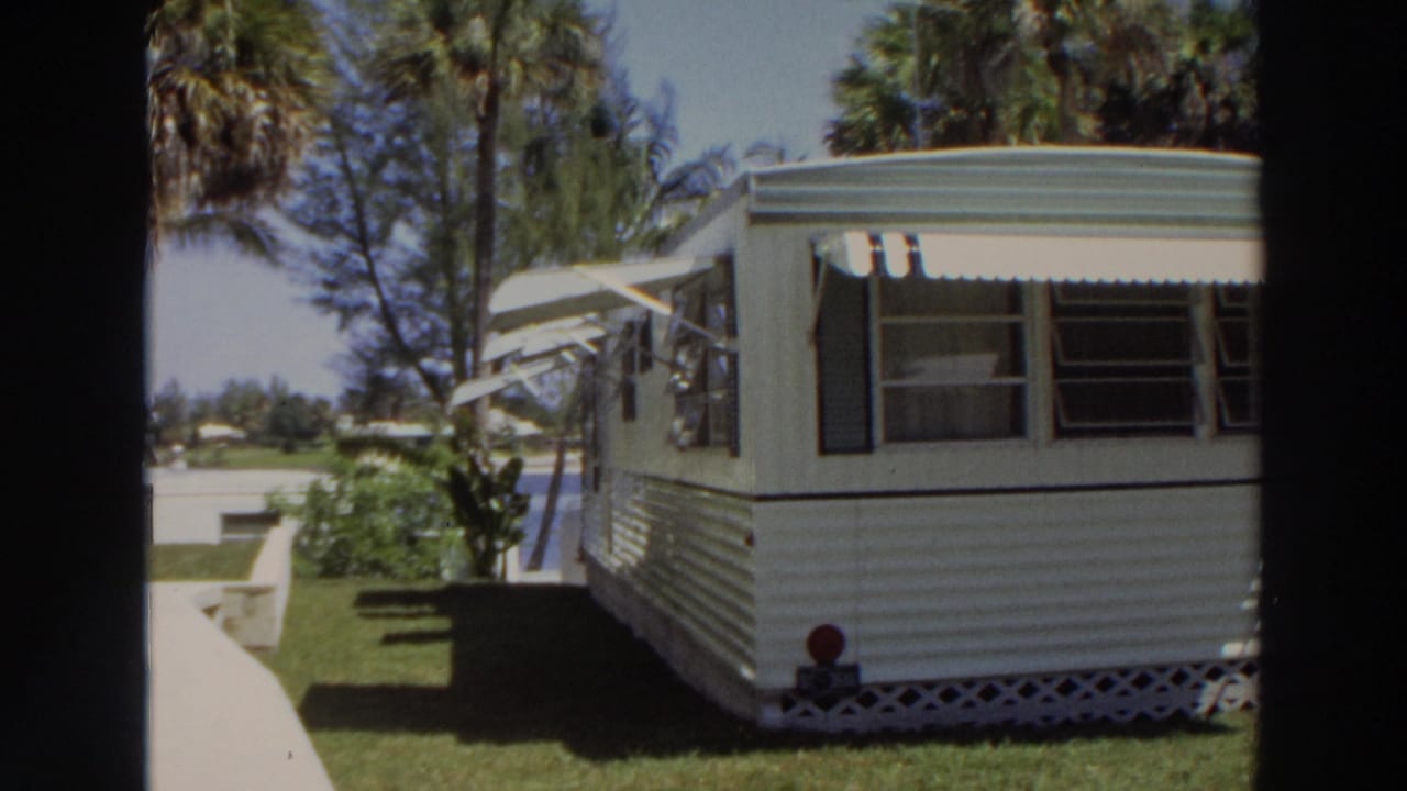 1966 Puerto Rico frame showing a mobile home at the edge of a walkway with palms, lawn, and lattice skirting.