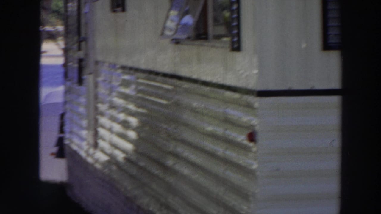 1966 Puerto Rico frame showing the side of a mobile home, small windows, striped awning, and dark porch framing in foreground.