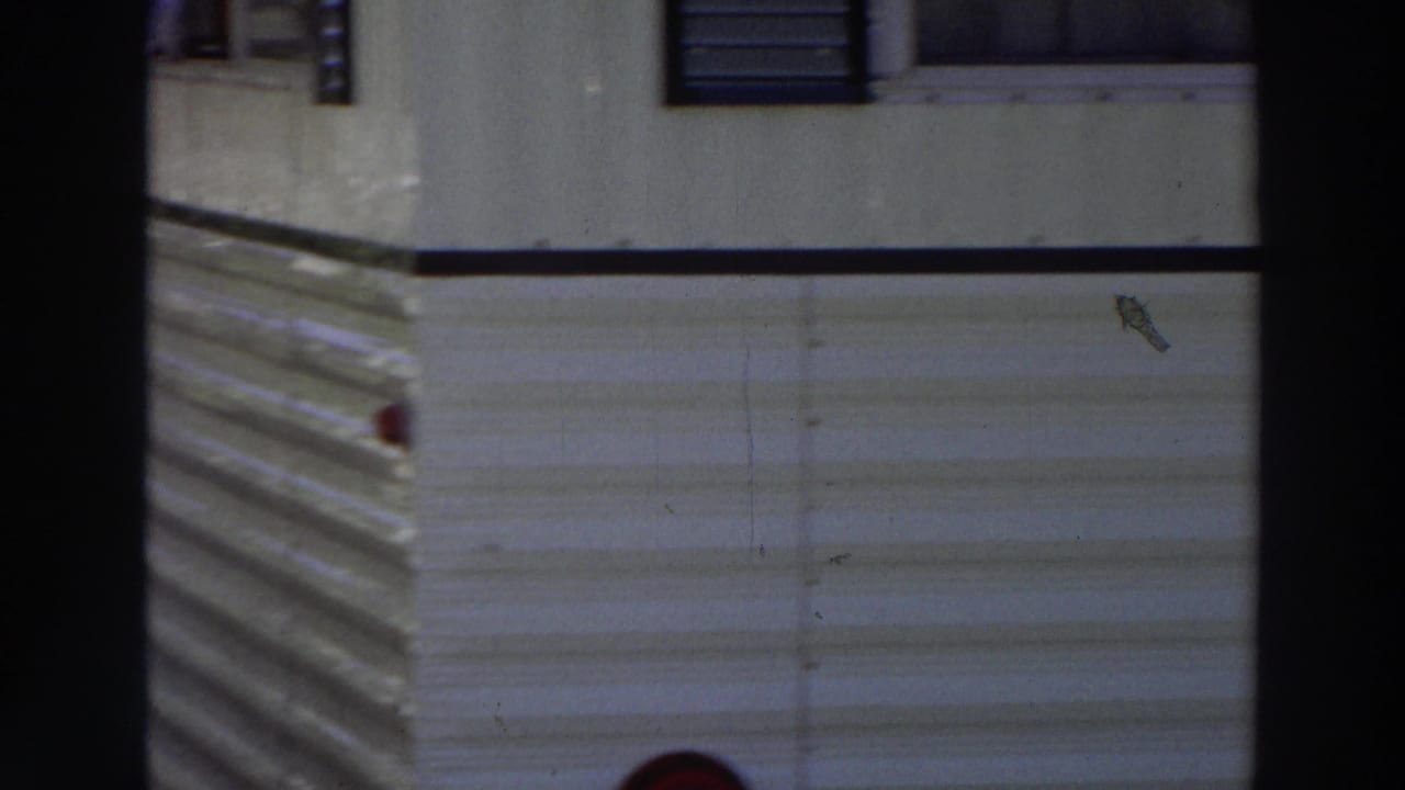 White mobile-home siding with dark window bars and a red side light.