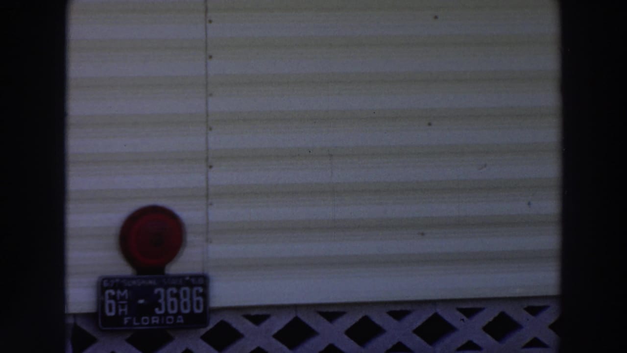 Rear section of a white mobile home with a Florida license plate and red light.