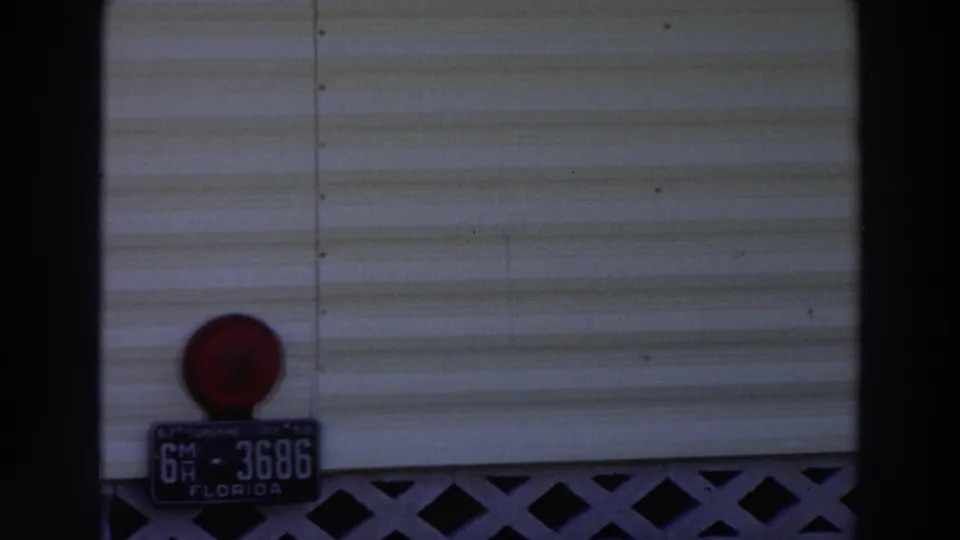 1966 Puerto Rico frame with a white mobile-home exterior, visible Florida license plate, red circular light, and lattice skirting.