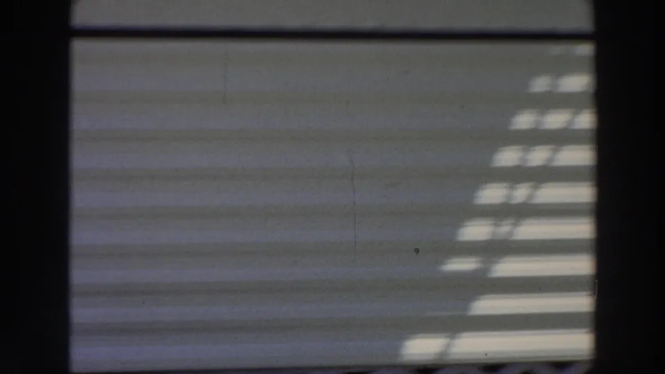 1966 Puerto Rico home-movie frame showing white mobile-home siding with sunlit shadow patterns and dark film-frame borders.