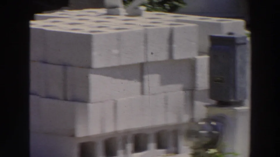 A Puerto Rico 1966 home-movie frame shows white cinder blocks near a roadside motel area, with handheld blur and sunlit exposure.