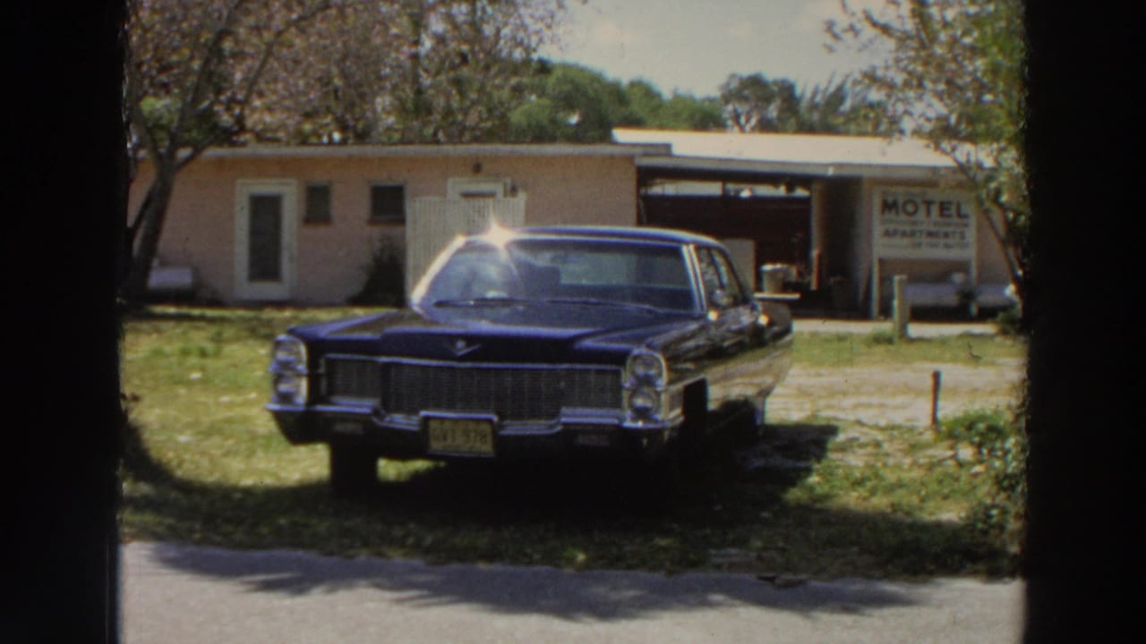 Dark blue sedan parked on grass near a motel-apartments sign.