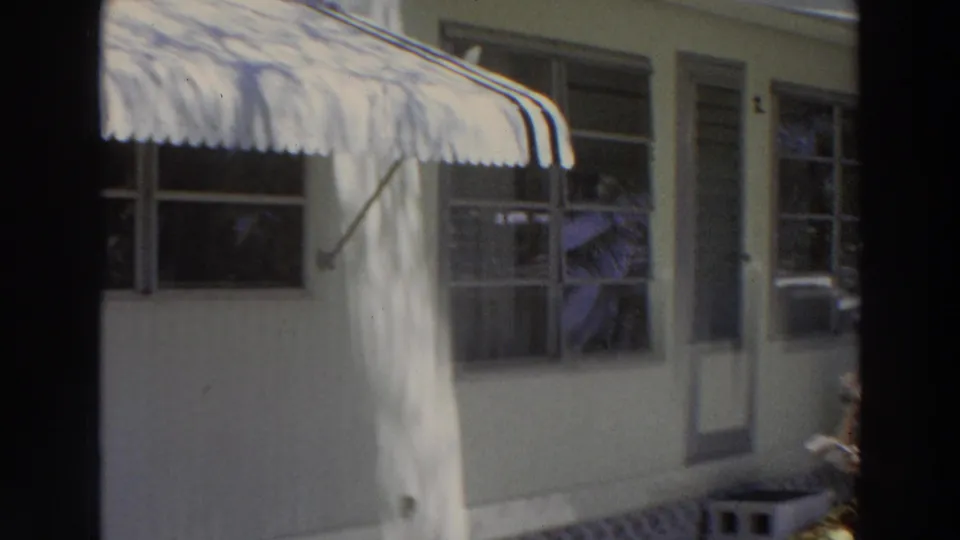 A motel porch in Puerto Rico shows striped awning, windows, and a woman seated inside or near the porch area, possibly reading.