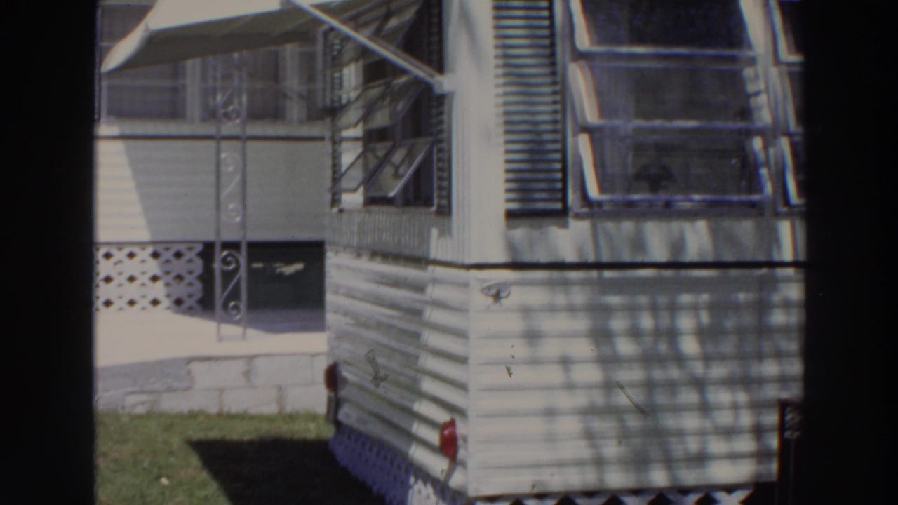 1966 Puerto Rico frame of a resort mobile home corner with white siding, shaded windows, awnings, and grass at the base.