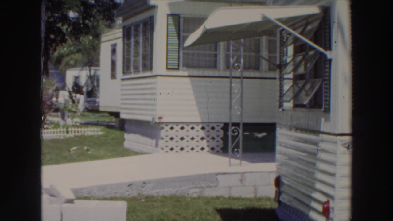 1966 Puerto Rico home-movie view of a white resort mobile home beside a driveway, with screened windows, awning, and lattice skirting.