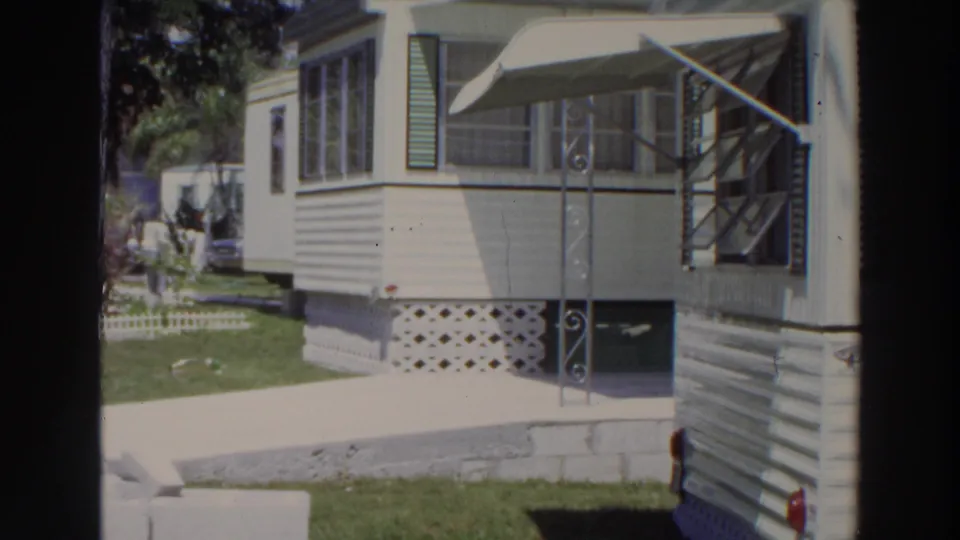 1966 Puerto Rico home-movie view of a white resort mobile home beside a driveway, with screened windows, awning, and lattice skirting.