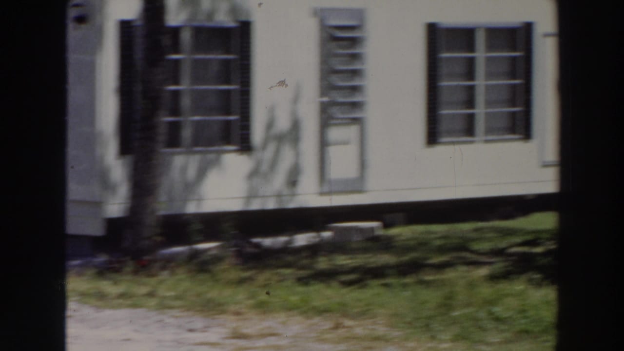 1966 Puerto Rico home-movie view of a light residential facade with windows, shutters, lawn, tree shadows, and a narrow paved path.