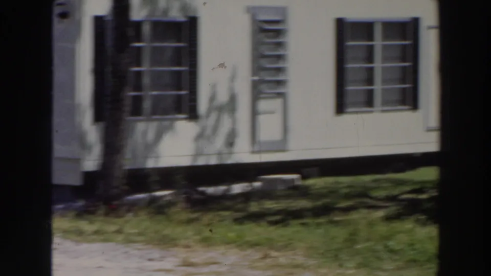 1966 Puerto Rico home-movie view of a light residential facade with windows, shutters, lawn, tree shadows, and a narrow paved path.