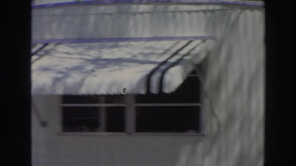 1966 Puerto Rico frame of a light-colored building exterior with a striped awning, dark windows, and shadows across the wall.
