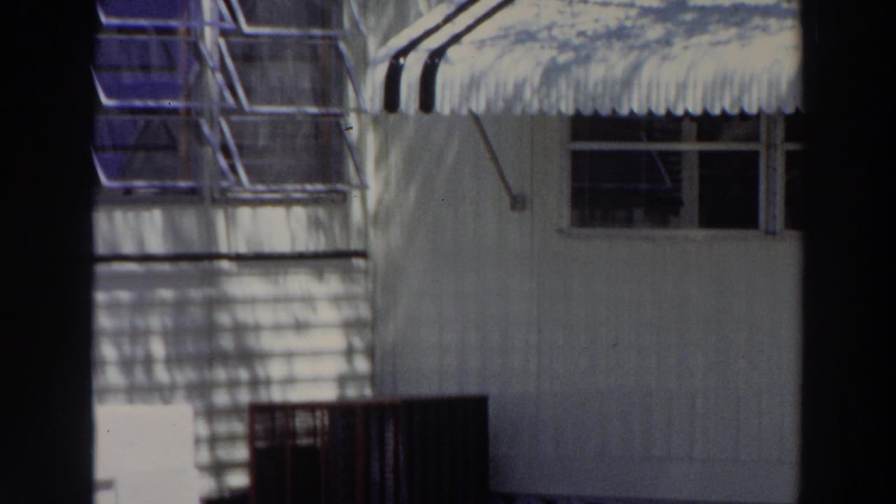 1966 Puerto Rico home-movie view of a building corner with striped awning, window openings, railing, and palm-like shadows.