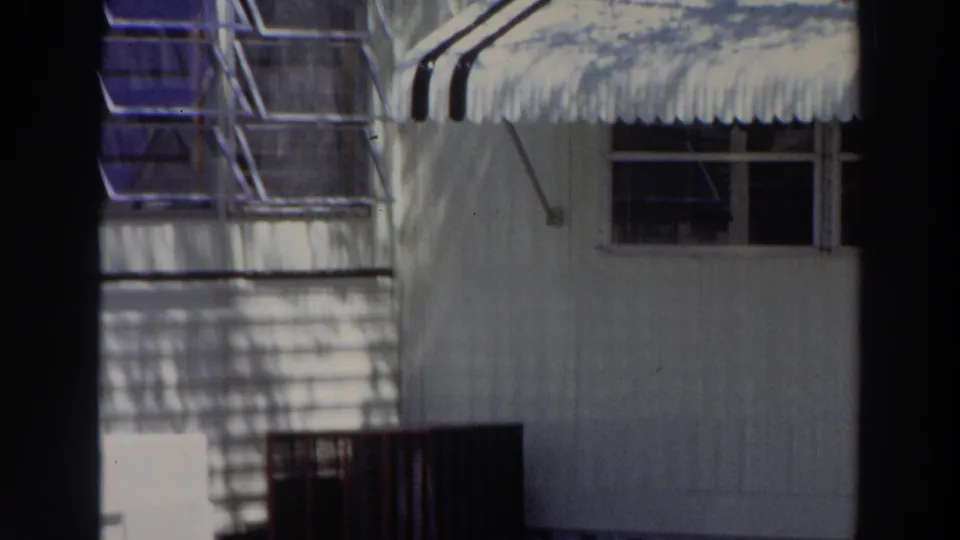 1966 Puerto Rico home-movie view of a building corner with striped awning, window openings, railing, and palm-like shadows.