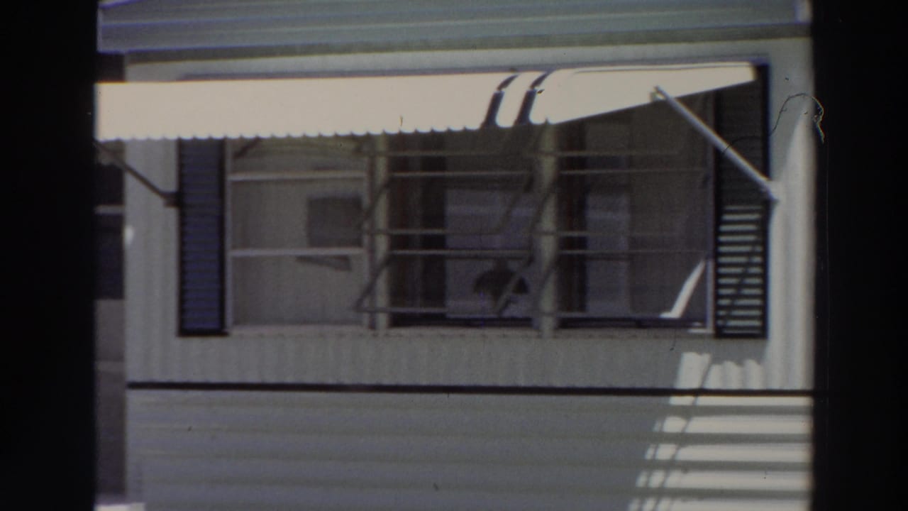 Pale building facade with white awning, louvered shutters, and dark foreground framing.