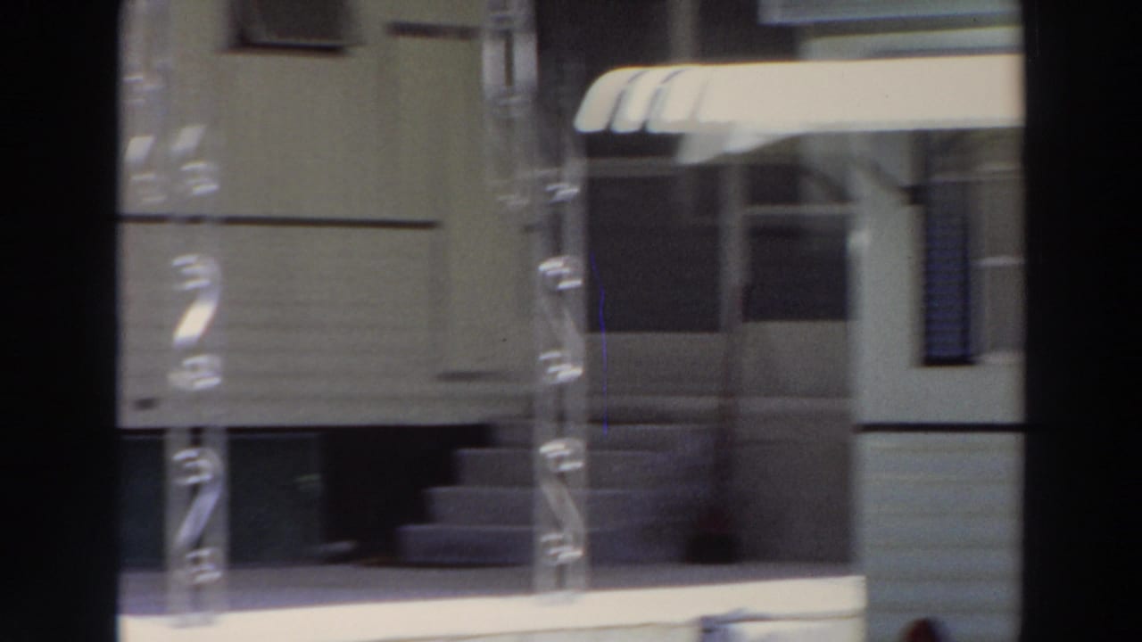 1966 Puerto Rico exterior frame showing a building entrance with a striped awning, metal porch supports, steps, and a shaded doorway.