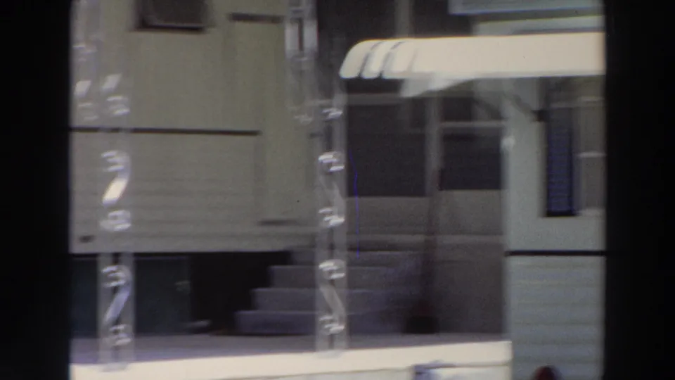 1966 Puerto Rico exterior frame showing a building entrance with a striped awning, metal porch supports, steps, and a shaded doorway.