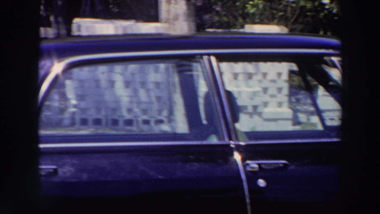 1966 Puerto Rico frame showing a dark blue classic car parked near a building, with patterned curtains or coverings visible through the windows.