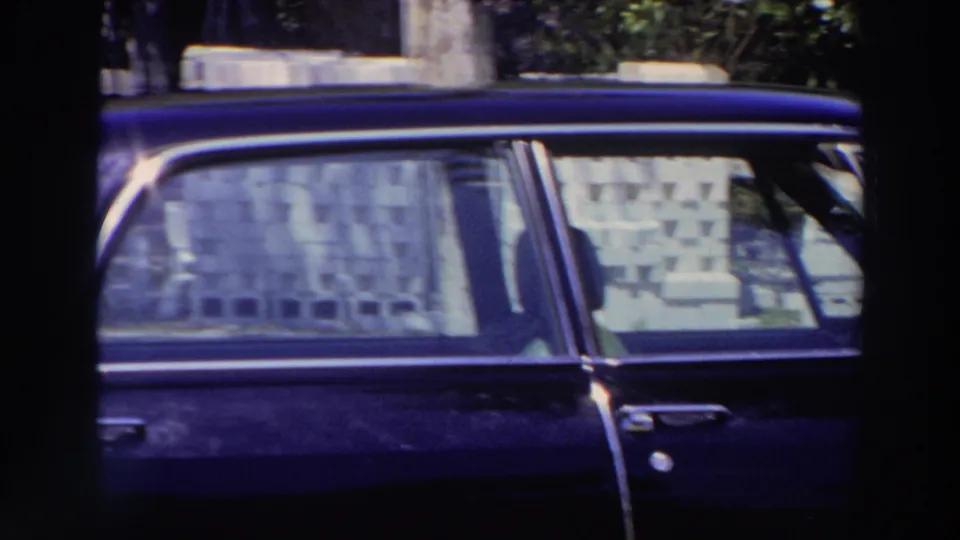 1966 Puerto Rico frame showing a dark blue classic car parked near a building, with patterned curtains or coverings visible through the windows.